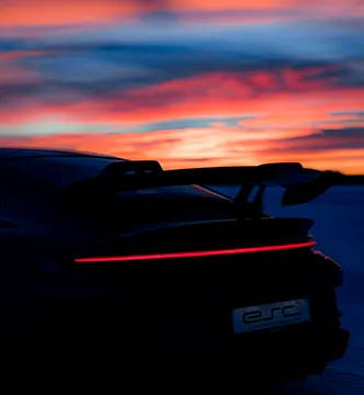 Die Silhouette eines Porsche mit leuchtendem Hecklichtband vor einem dramatischen Sonnenuntergang bei einem ESC Icedriving-Event.

