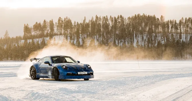 Ein blauer Porsche 911 GT3 des ESC European Speed Club driftet bei einem Icedriving-Event vor einer Waldkulisse in Schweden.