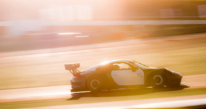 Ein Porsche 911 Rennwagen des ESC European Speed Club fährt bei Sonnenuntergang mit hoher Geschwindigkeit über die Rennstrecke.

