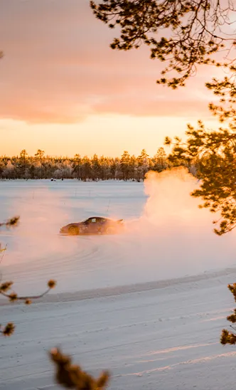 Ein Sportwagen des ESC European Speed Club driftet bei Sonnenuntergang durch eine verschneite Landschaft in Schweden.

