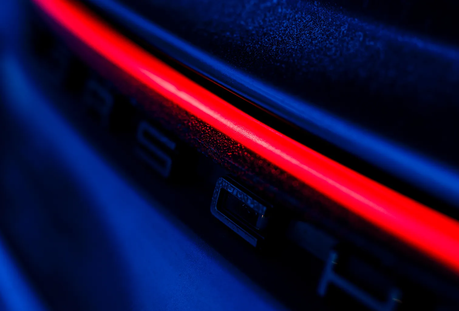 Nahaufnahme eines roten Rücklichts an einem schwarzen Fahrzeug in dunkler Umgebung mit blauem Licht.