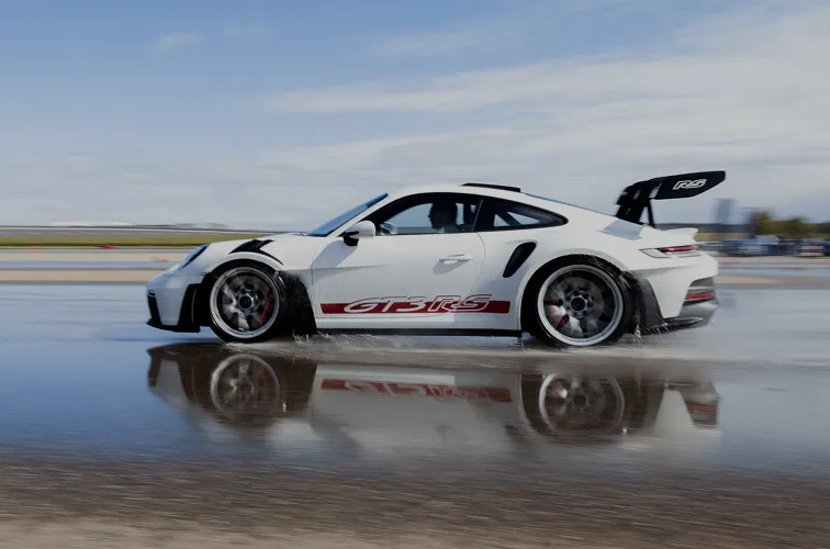 Weißer Porsche GT3 RS fährt auf nasser Strecke mit Wasserspritzern und Reflexion auf dem Boden.