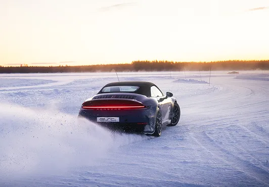Ein Sportwagen fährt auf einer verschneiten und vereisten Strecke bei Sonnenuntergang und wirbelt Schnee auf.
