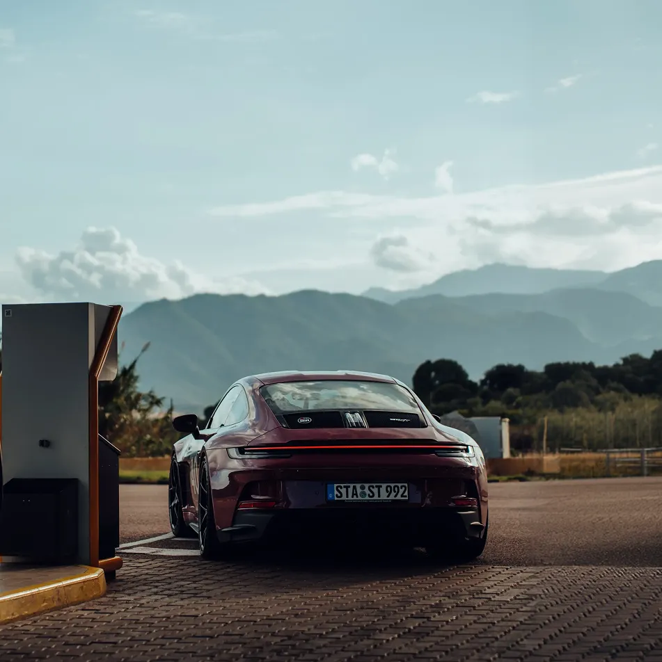 Roter Sportwagen Porsche lädt an einer Station mit Bergen im Hintergrund.