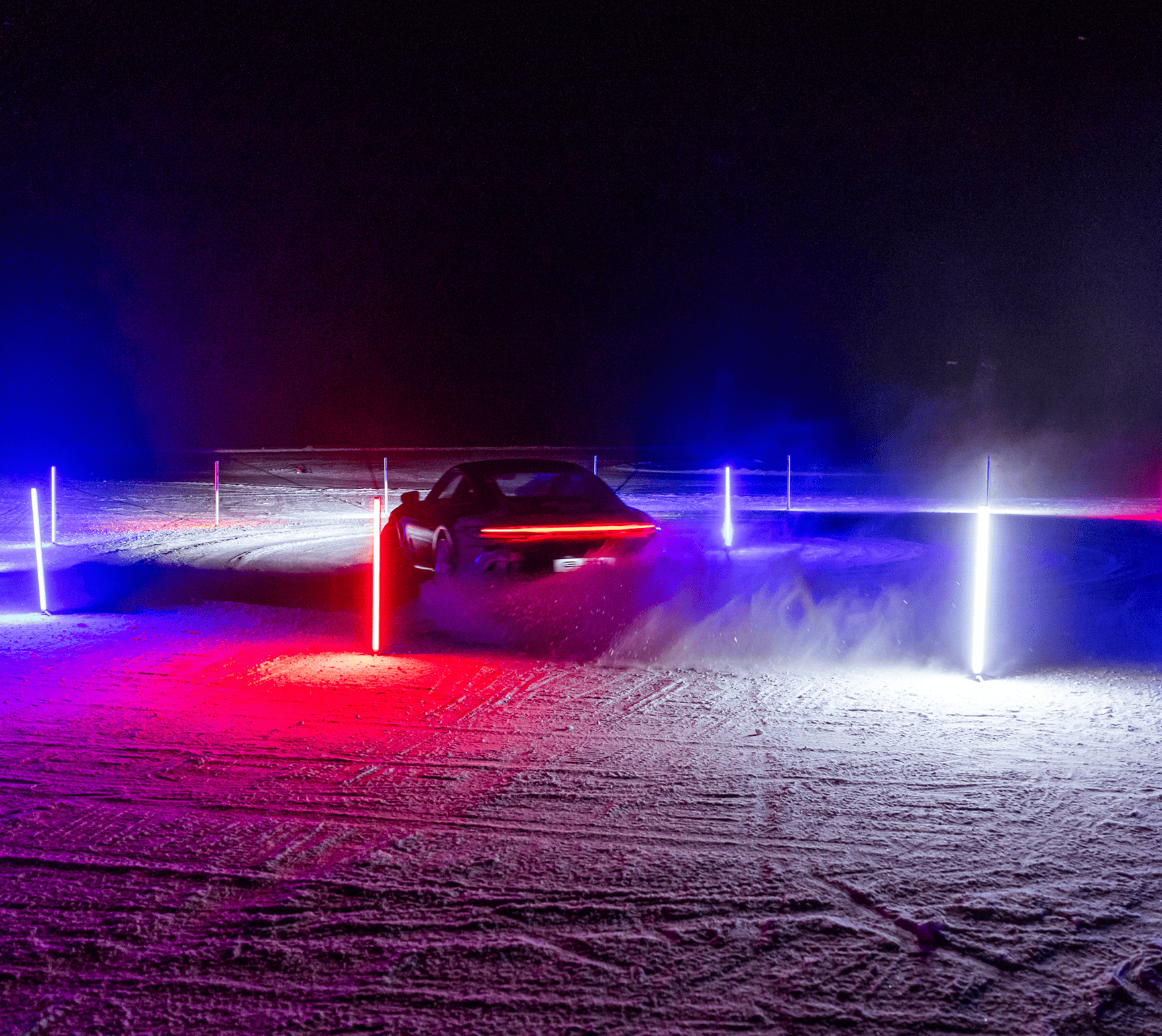 Sportwagen fährt nachts auf einer verschneiten Strecke, umgeben von roten und blauen Leuchtpfosten.