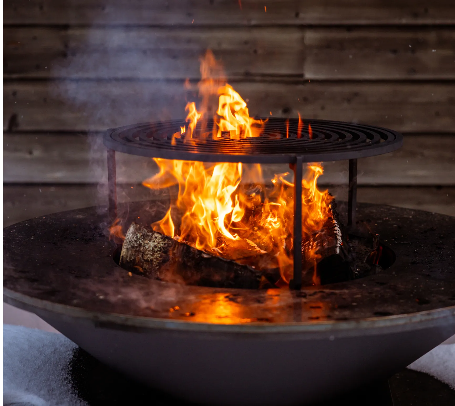 Feuer brennt in einem Grill mit runden Metallstäben, Holzscheite glühen im Inneren.