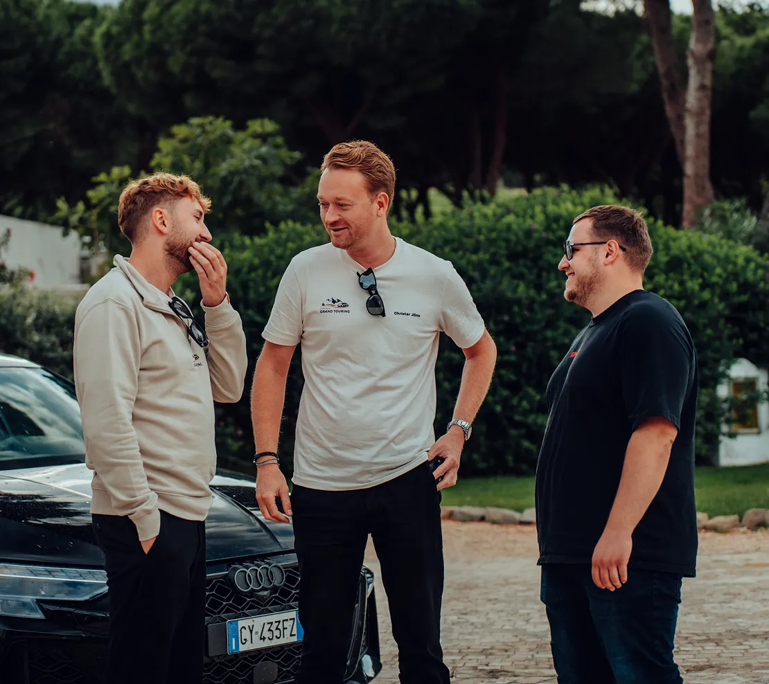 Three men are standing outside a black Audi and talking laughing.