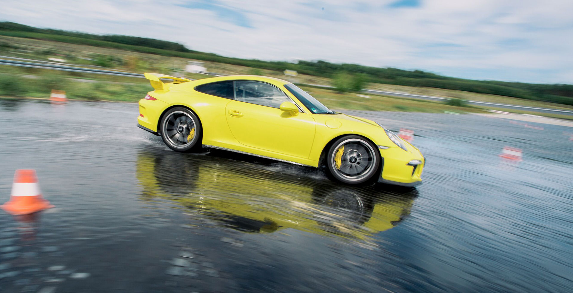 Gelber Sportwagen, der schnell auf nasser Fahrbahn mit Verkehrshütchen fährt.