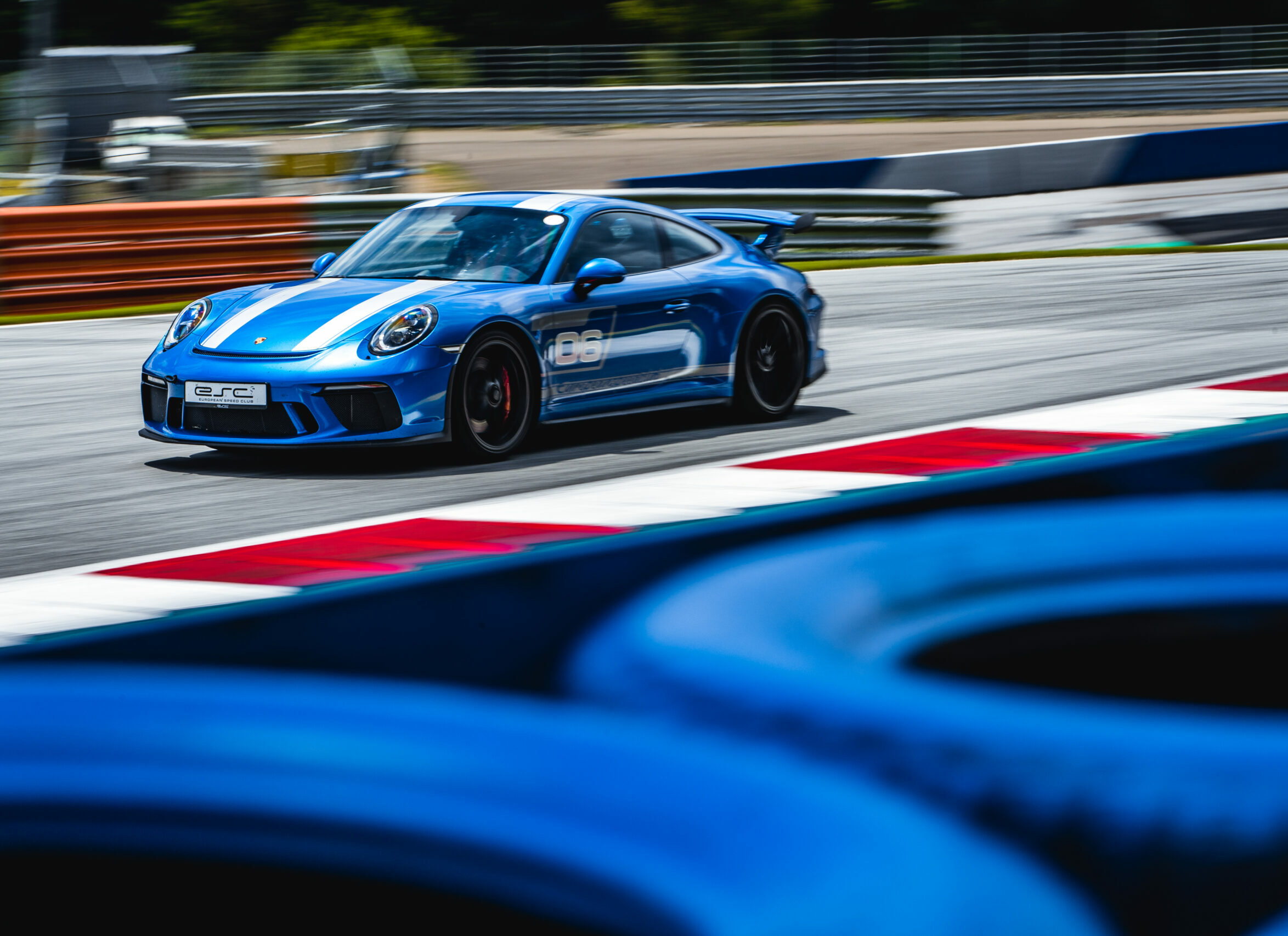 Blauer Porsche-Rennwagen mit weißen Streifen fährt schnell auf einer Rennstrecke an roten und weißen Curbs vorbei.
