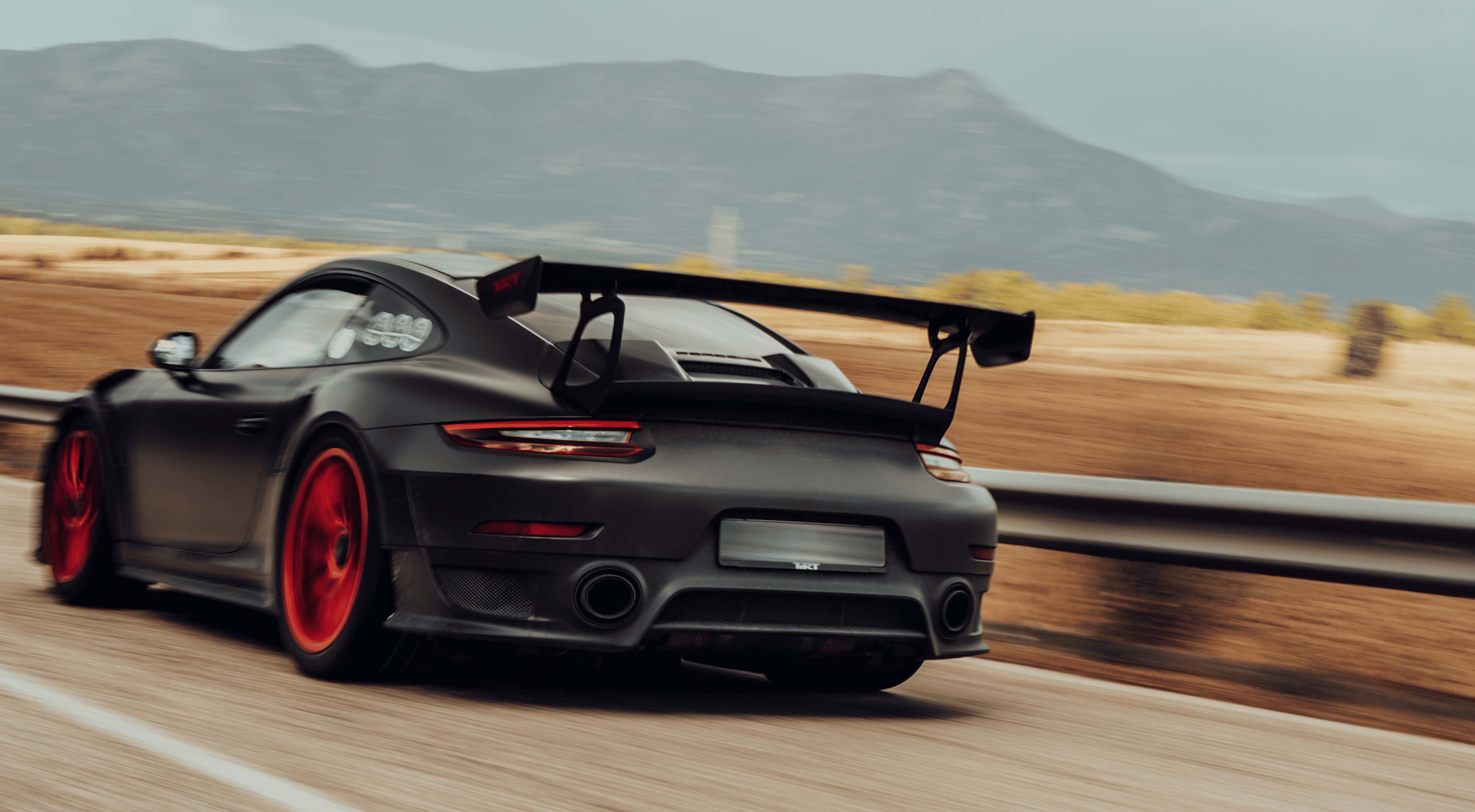 Schwarzer Sportwagen mit rotem Rad fährt auf einer Bergstraße mit unscharfem Hintergrund.