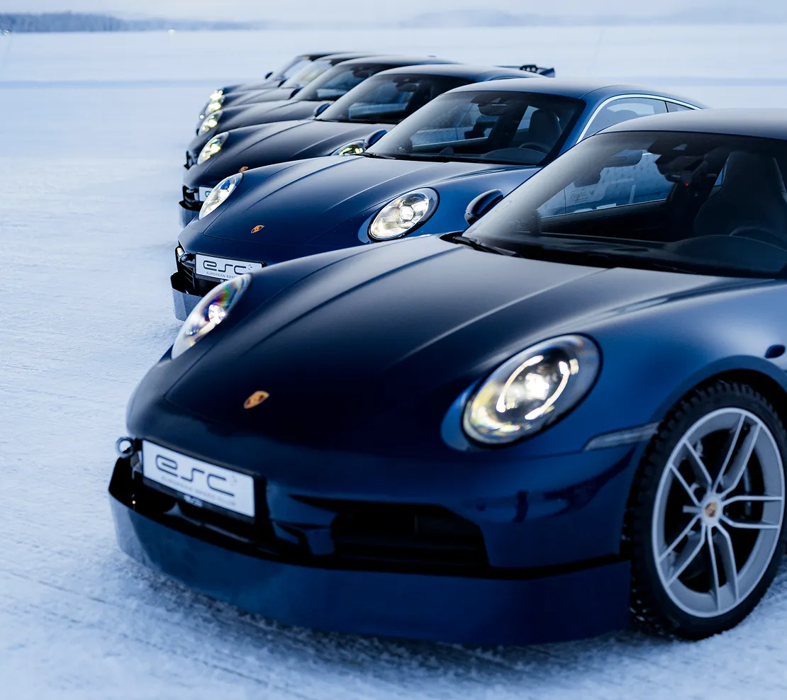 Eine Reihe von dunkelblauen Porsche-Sportwagen, nebeneinander auf einer verschneiten Fläche geparkt.