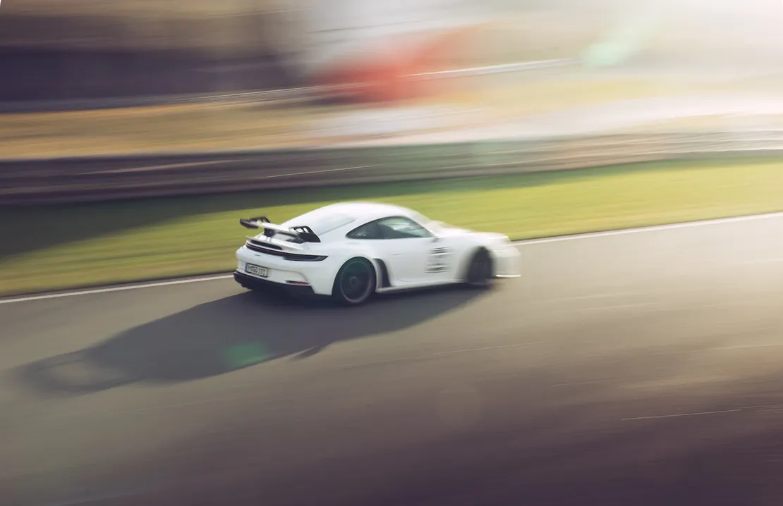 Weißer Sportwagen mit Heckflügel fährt schnell auf einer Rennstrecke bei Sonnenlicht.