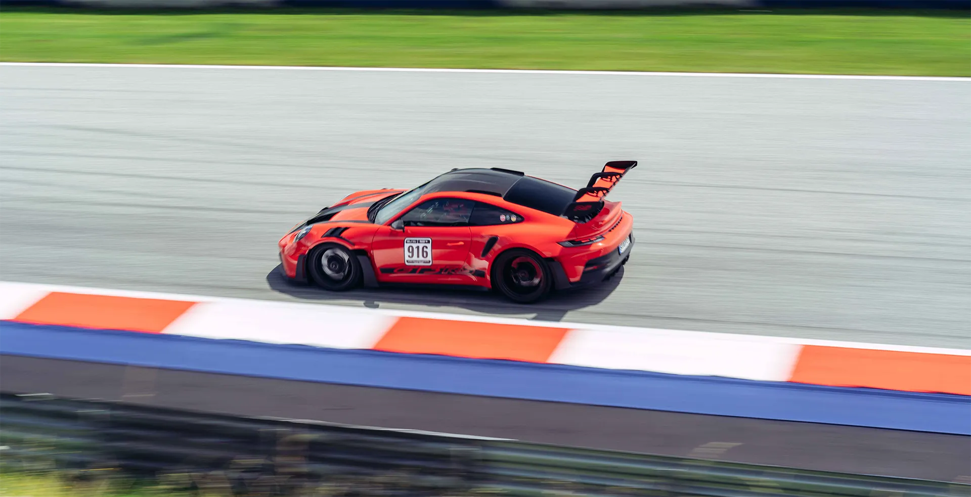 Rotes Rennsportauto mit Nummer 916 auf einer Rennstrecke mit grünem Hintergrund.