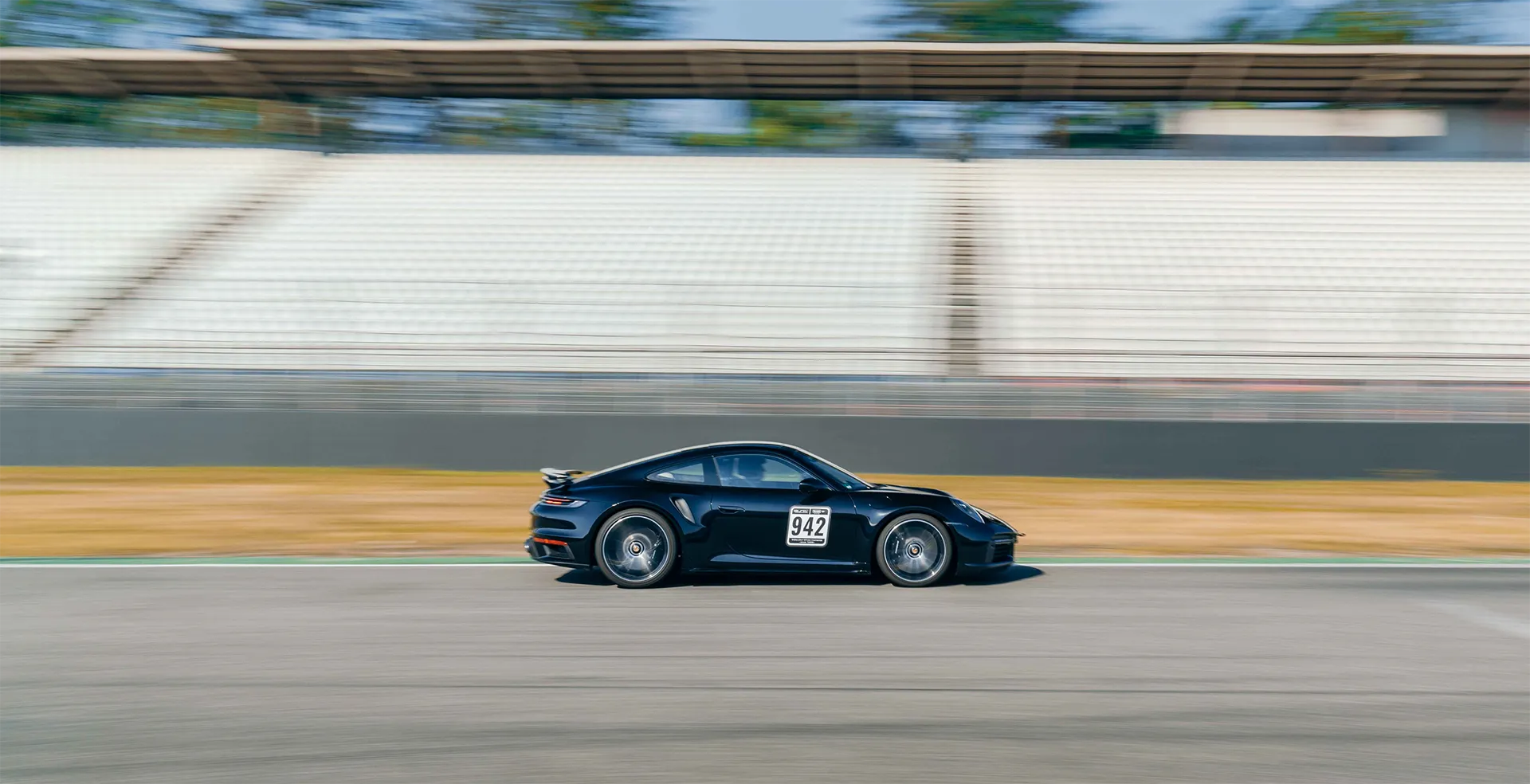 Schwarzer Rennwagen mit der Nummer 942 fährt schnell auf einer Rennstrecke vor leeren Tribünen.