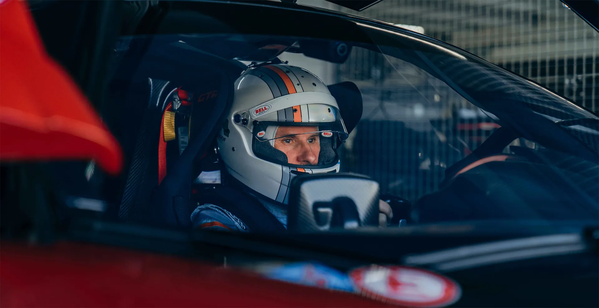 Rennfahrer mit weißem Helm und blauem Overall sitzt konzentriert im Rennwagen.