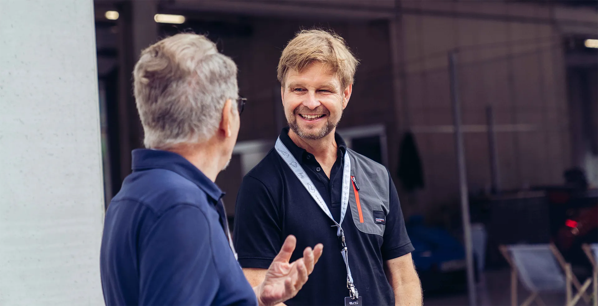 Zwei Männer unterhalten sich, einer mit grauem Haar und Brille, der andere lächelt mit Ausweis um den Hals.