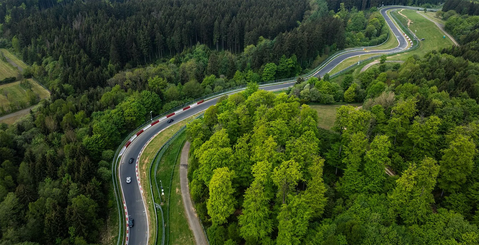 Luftaufnahme einer kurvigen Rennstrecke durch einen dichten grünen Wald mit mehreren Autos darauf.
