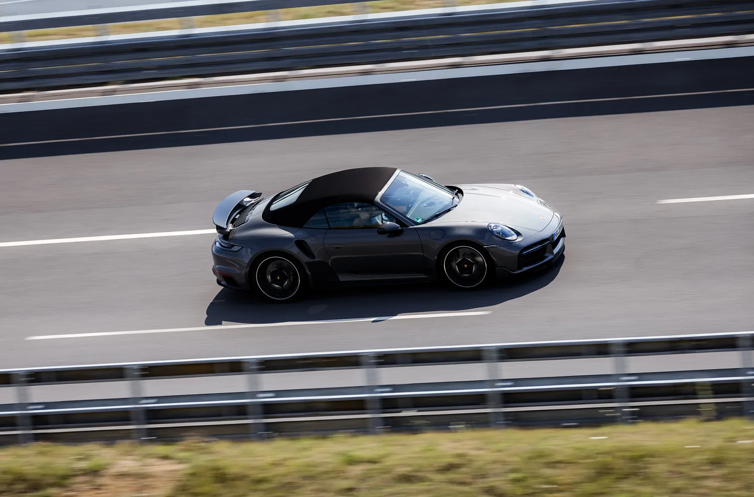 Dunkelgrauer Sportwagen mit schwarzem Verdeck fährt auf einer Autobahn mit weißen Fahrbahnmarkierungen.
