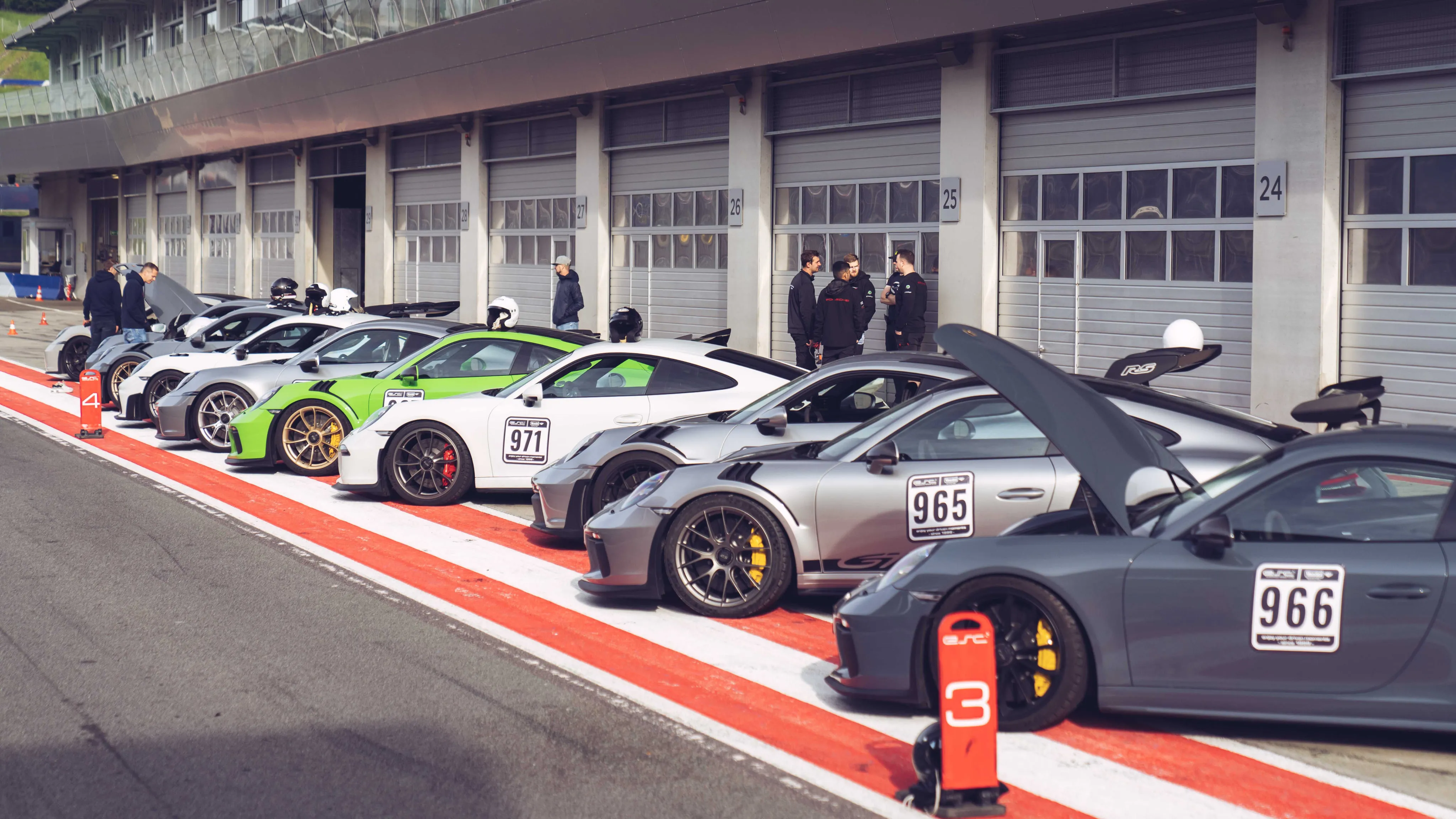 Mehrere Porsche-Sportwagen mit Rennnummern nebeneinander in der Boxengasse einer Rennstrecke geparkt.