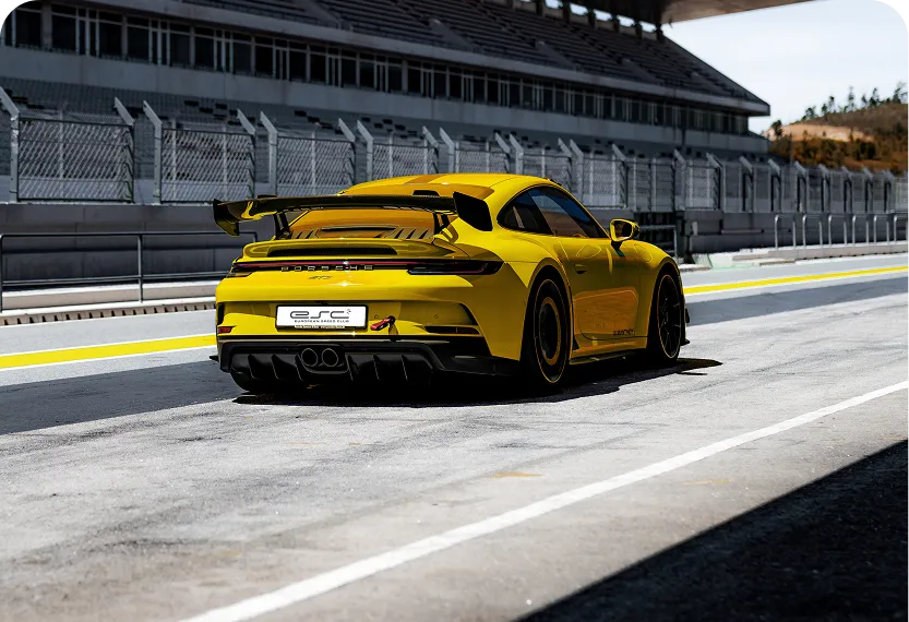 Gelber Porsche 911 GT3 auf einer Rennstrecke mit Tribüne im Hintergrund.