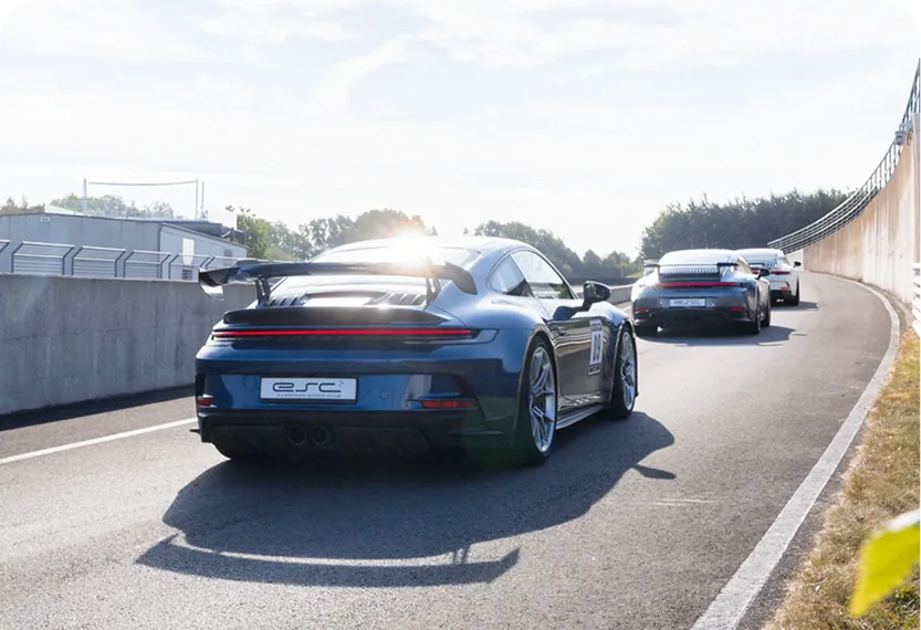 Drei Sportwagen fahren auf einer Rennstrecke, der vorderste ist ein blauer Porsche mit großem Heckspoiler.