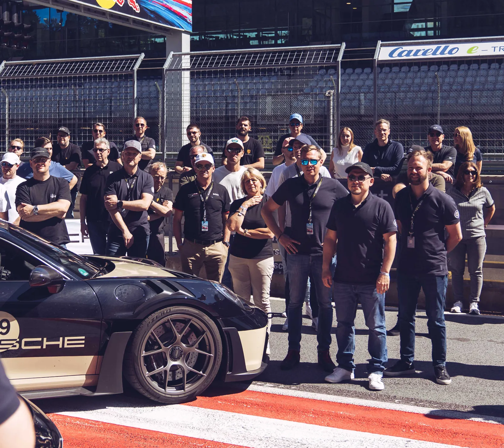 Gruppe von Menschen steht neben einem Rennwagen auf einer Rennstrecke mit rot-weißen Markierungen.