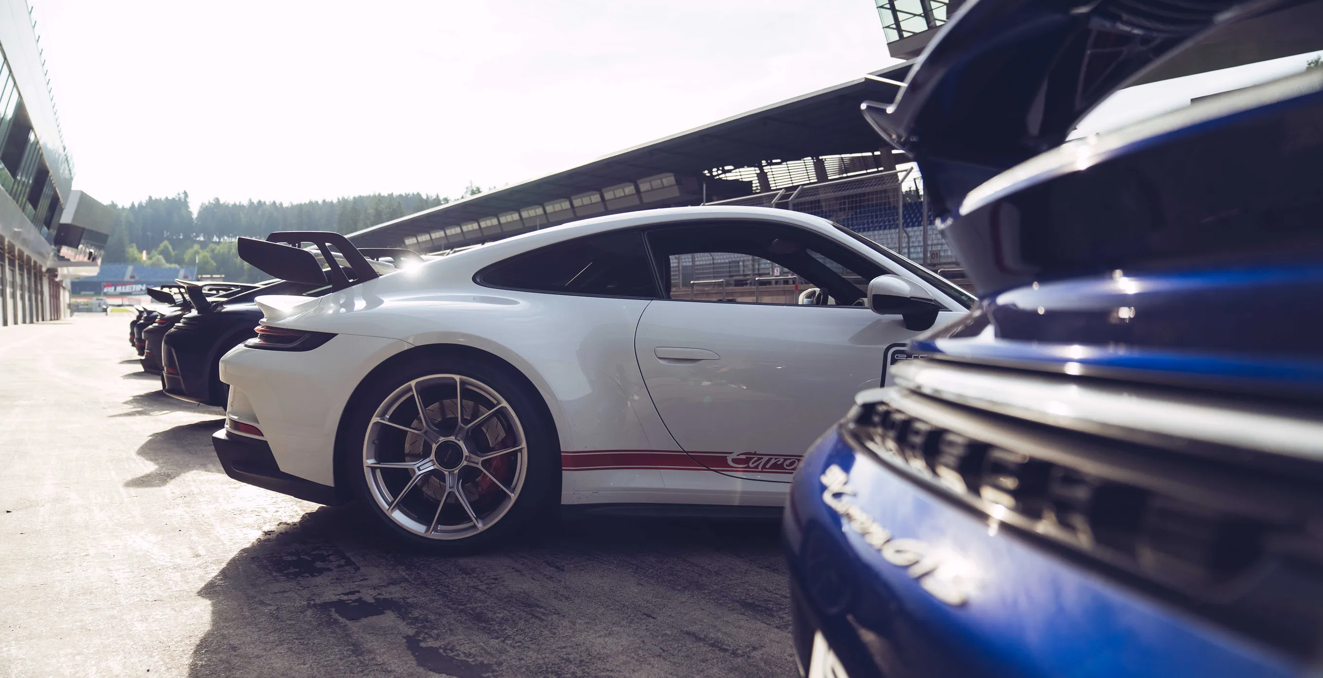 Weiße und schwarze Sportwagen mit Heckflügeln auf einer Rennstrecke parken nebeneinander.