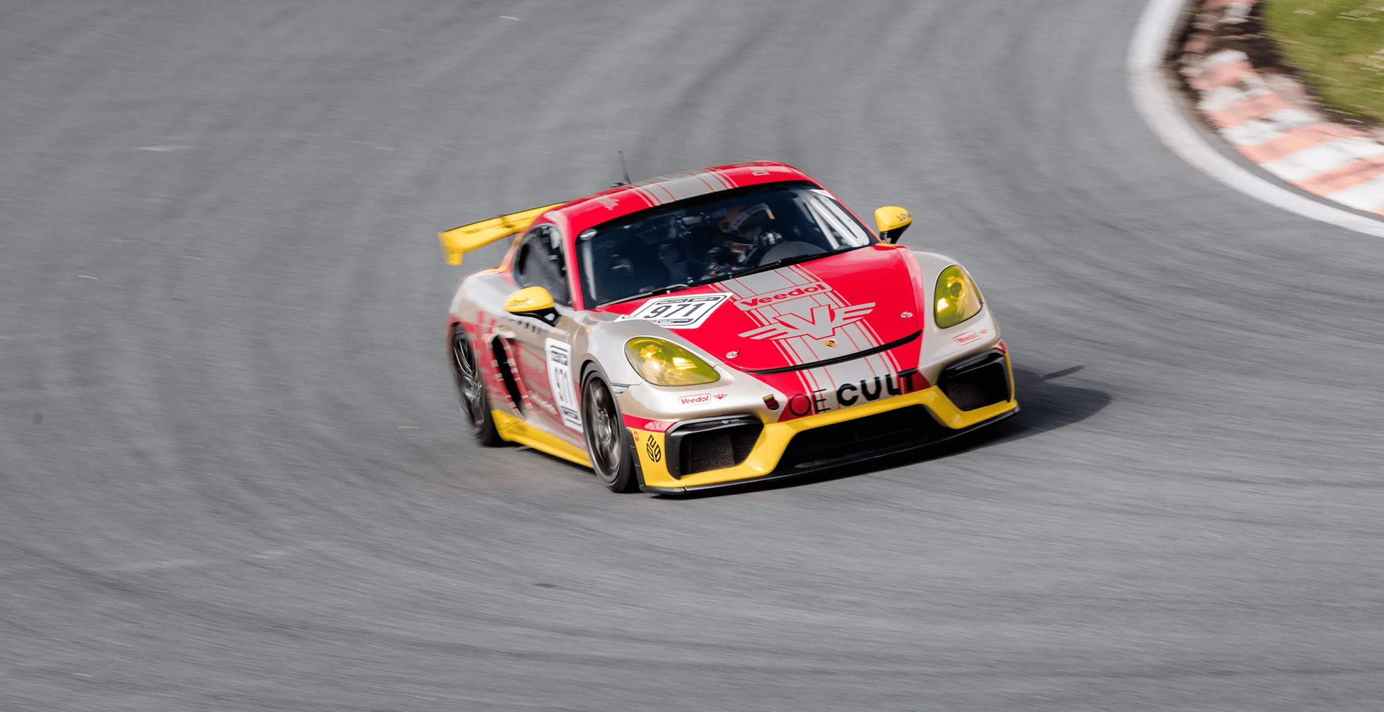Rennwagen mit rot-gelber Lackierung fährt auf einer kurvigen Rennstrecke.