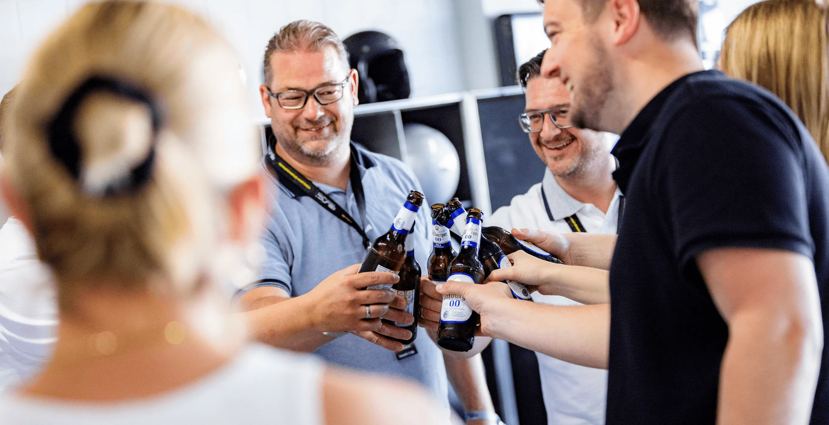 Gruppe von Menschen, die sich mit Flaschen alkoholfreien Biers zuprosten und lächeln.