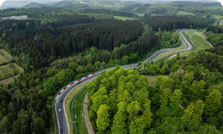 Luftaufnahme einer kurvenreichen Straße, die durch einen dichten grünen Wald in einer hügeligen Landschaft führt.