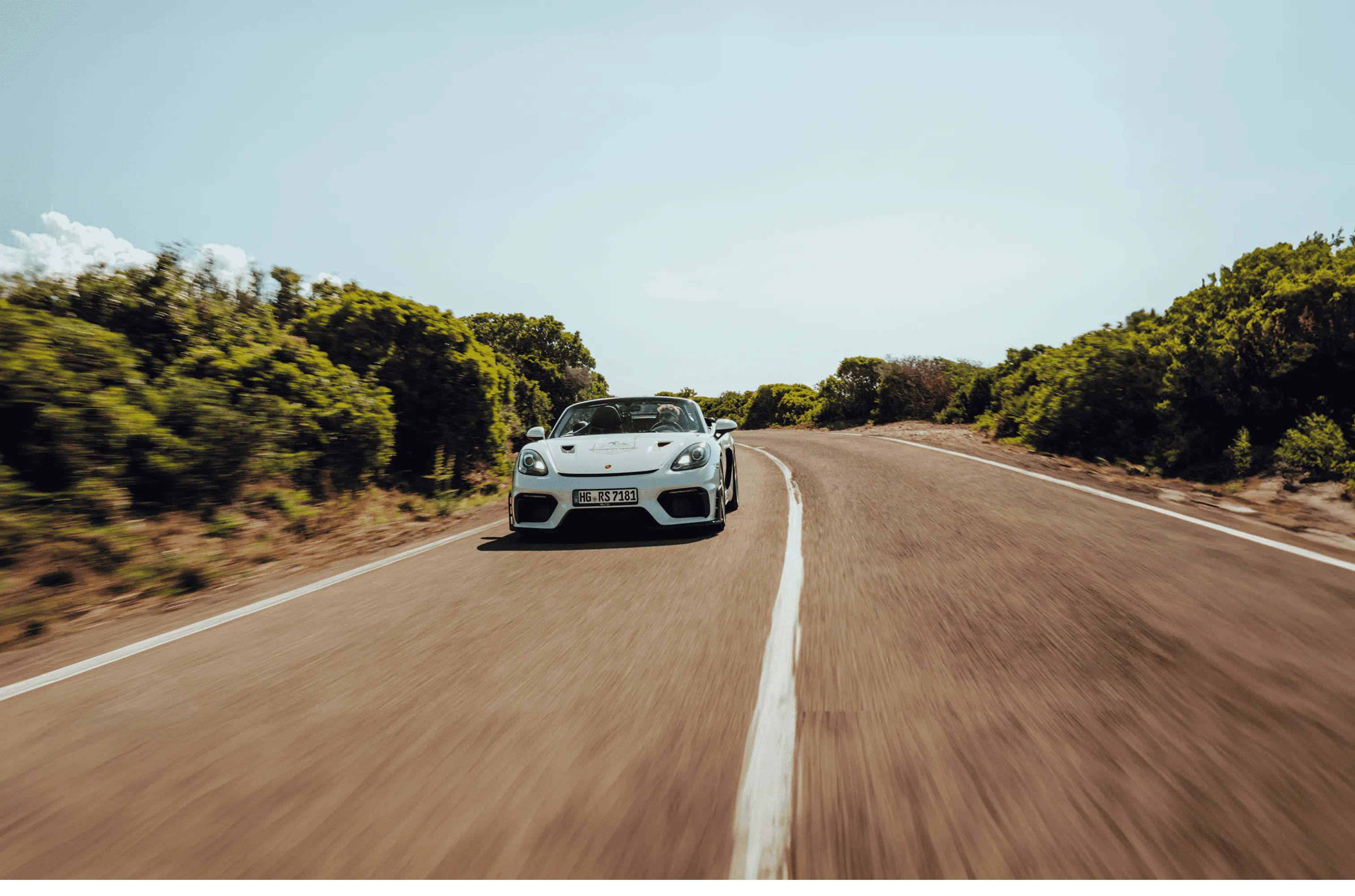 Weißes Sportcabrio fährt auf einer kurvigen Landstraße mit grünen Büschen an beiden Seiten.