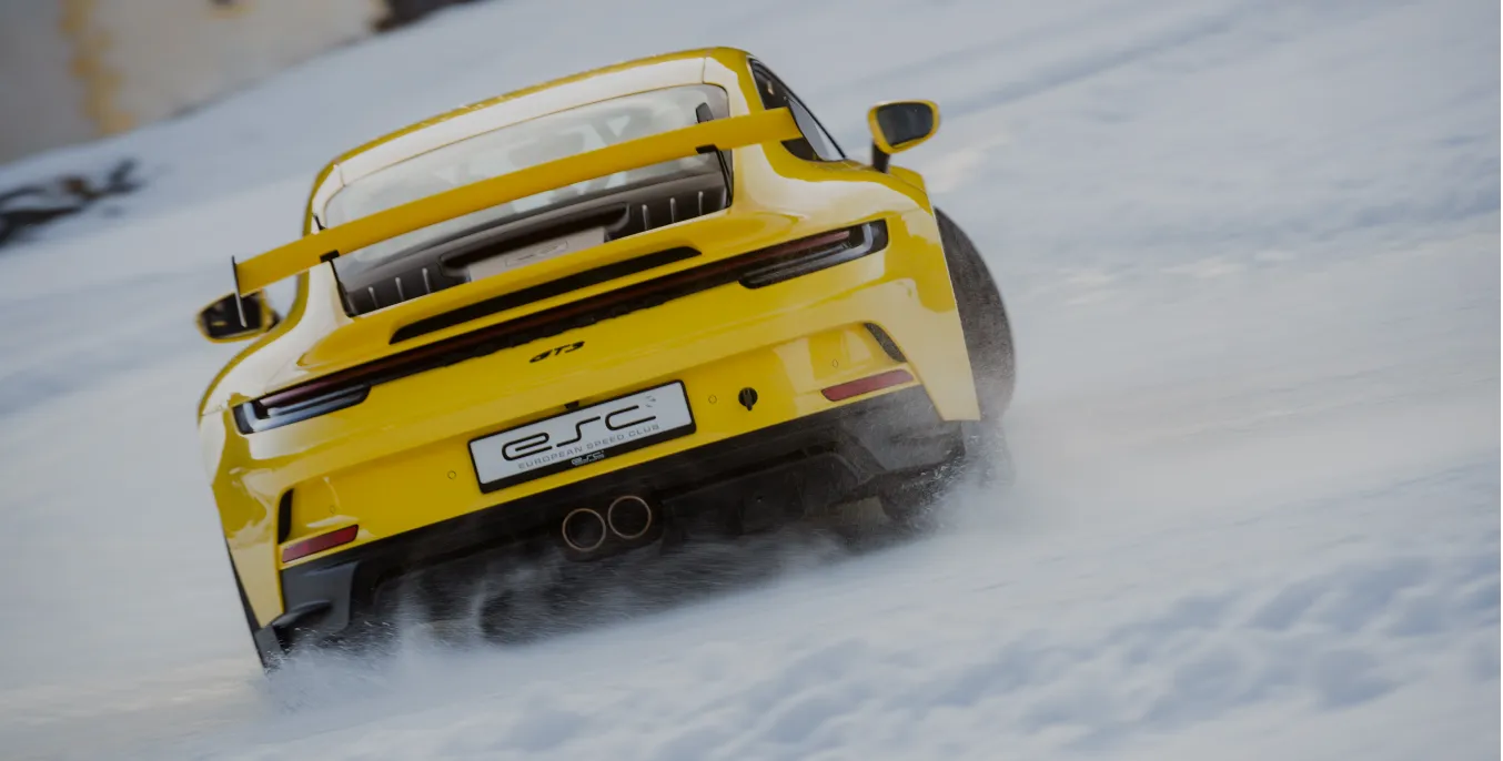 Ein gelber Porsche 911 GT3 fährt auf schneebedeckter Straße, Schnee spritzt seitlich.