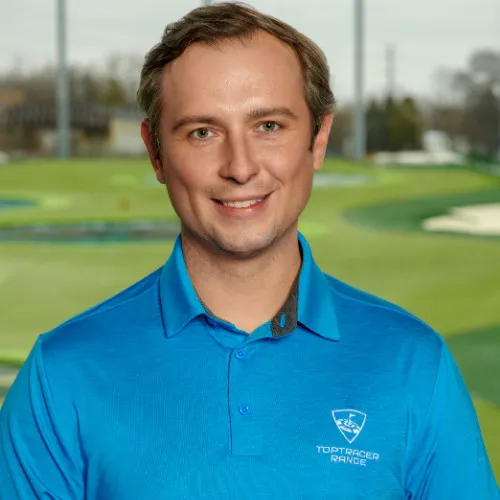 Smiling man wearing a blue Toptracer Range polo shirt standing outdoors on a golf driving range.