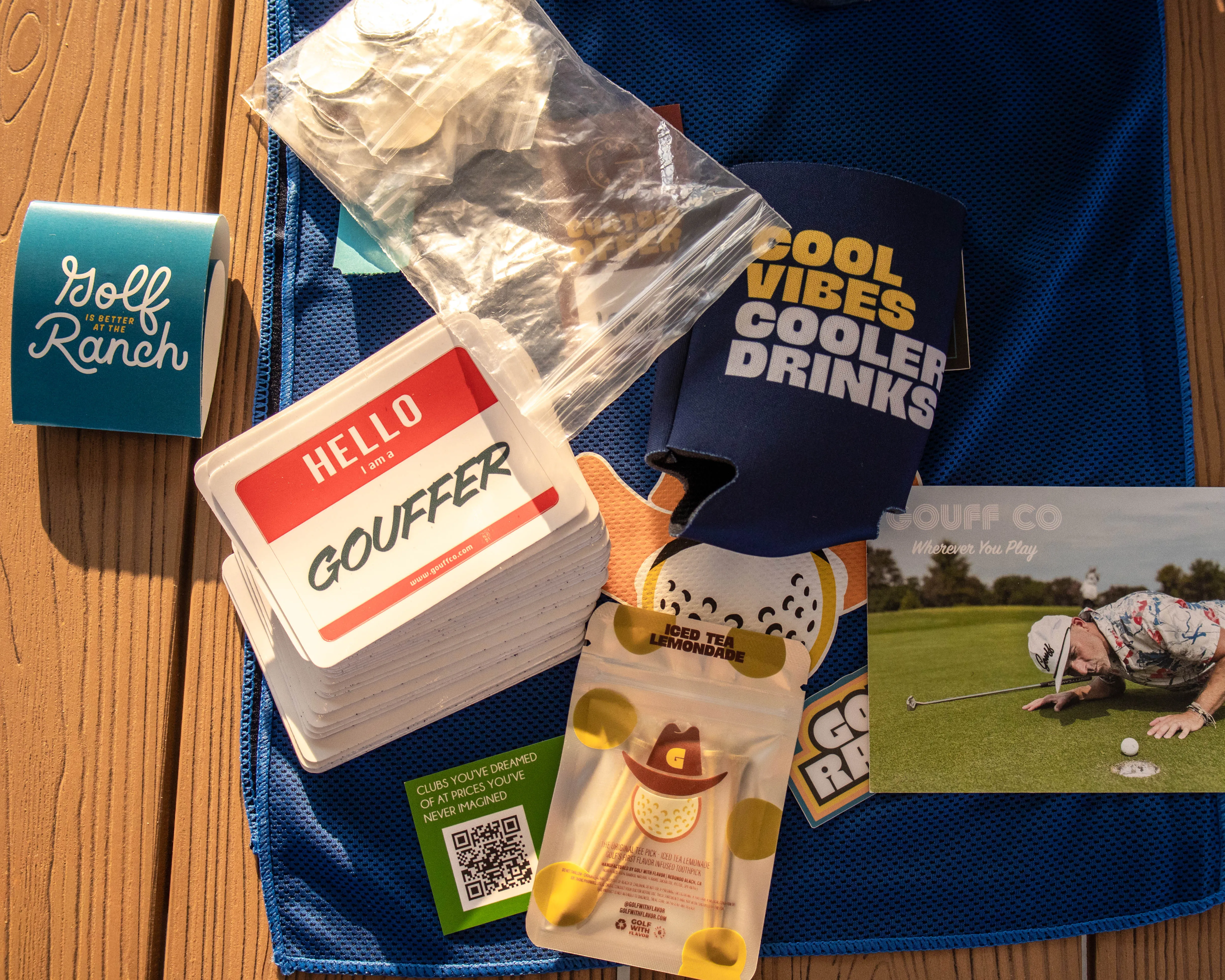 Golf-themed items on blue cloth including name tags, coins, drink cooler, stickers, and a golf postcard.