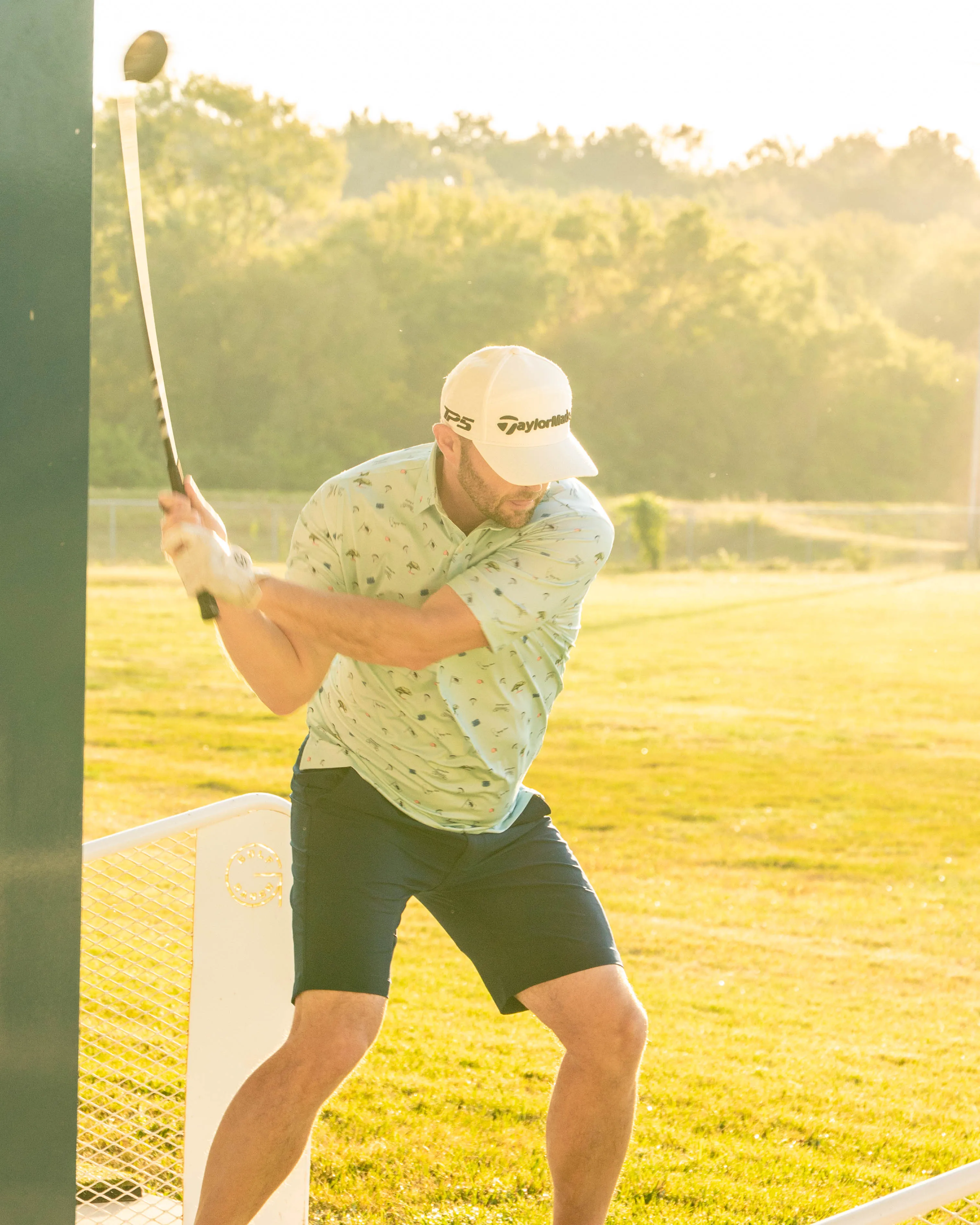 Man in golf attire preparing to swing a club at a sunny outdoor driving range.