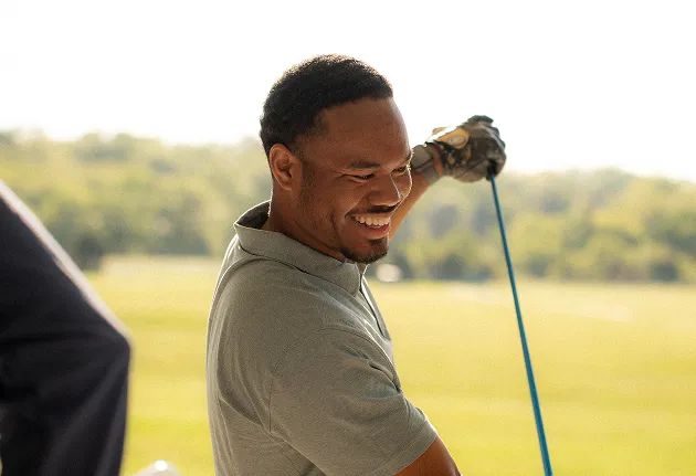 Smiling man holding a golf club on a green golf course.