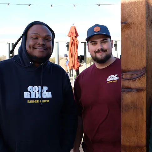 Two men smiling, one in black hoodie and one in maroon shirt with Golf Ranch logos outdoors.