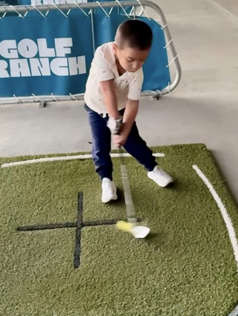 Young golfer hitting a ball on a practice mat at Golf Ranch