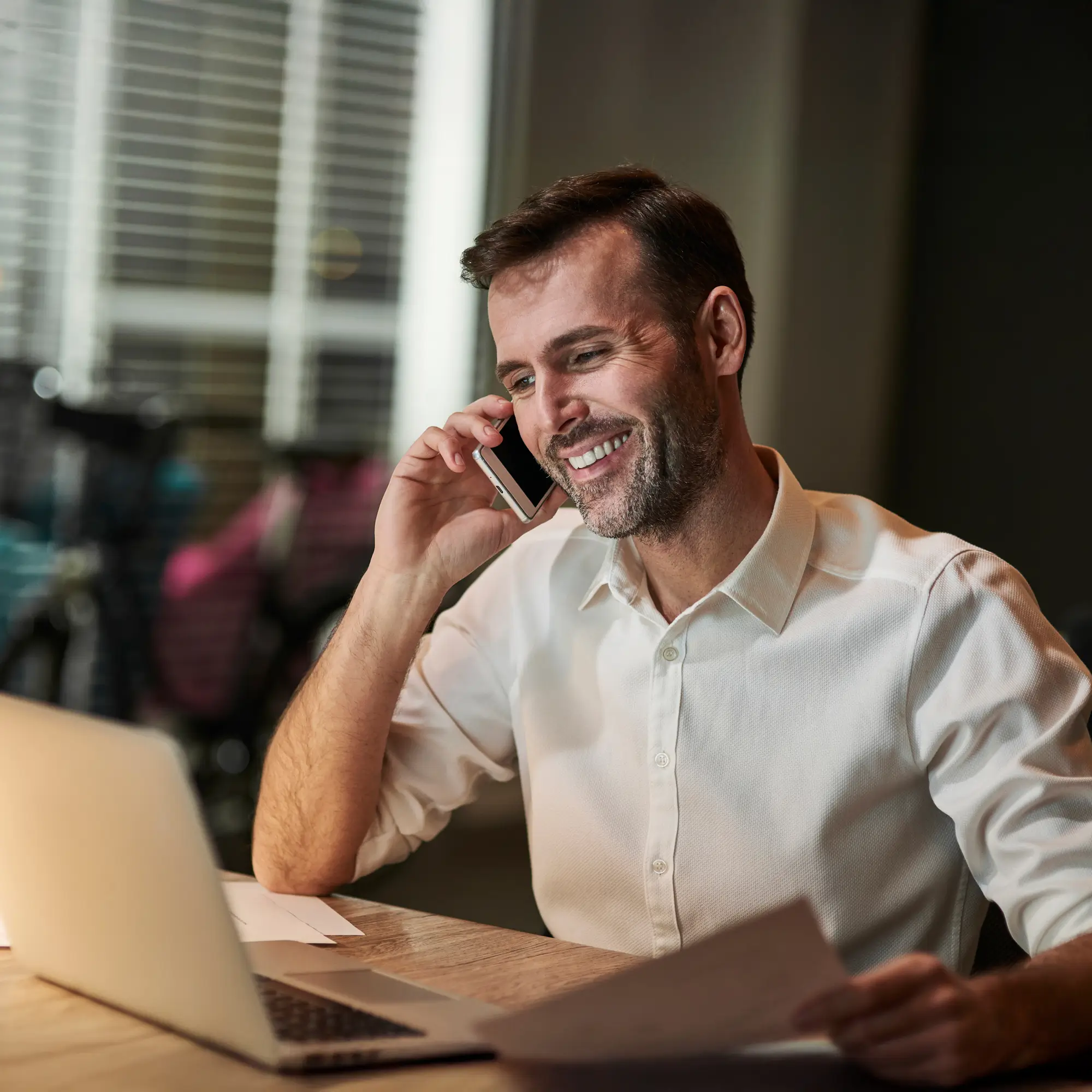 Smiling financial analyst on a phone call while reviewing documents at home.