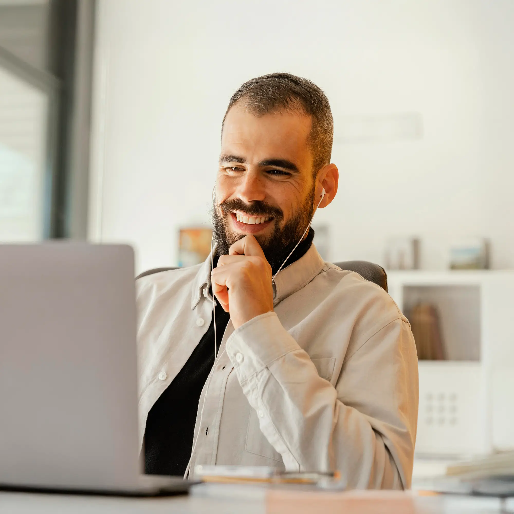 Professional offshore sales representative with earbuds smiling during client call in bright workspace
