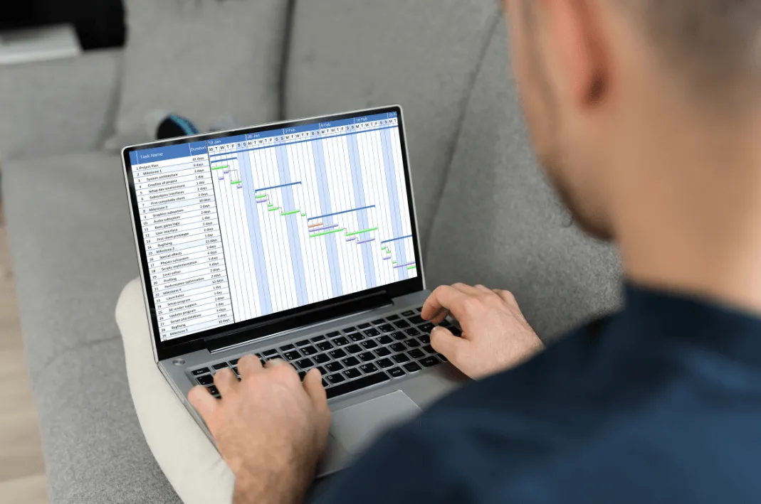 A man, offscreen, views his project timeline on his laptop.