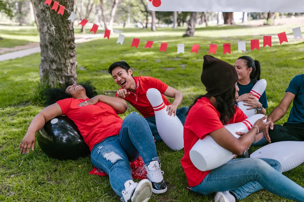 A team lounging and laughing in the park with inflatable bowling bowls and pins