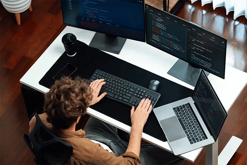 Professional nearshore developer coding on multiple monitors showcasing remote work efficiency for US companies