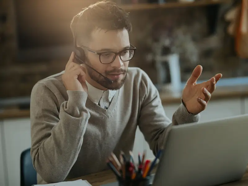 Male B2B sales professional on headset call gesturing while working on laptop showcasing Somewhere's world-class remote sales talent