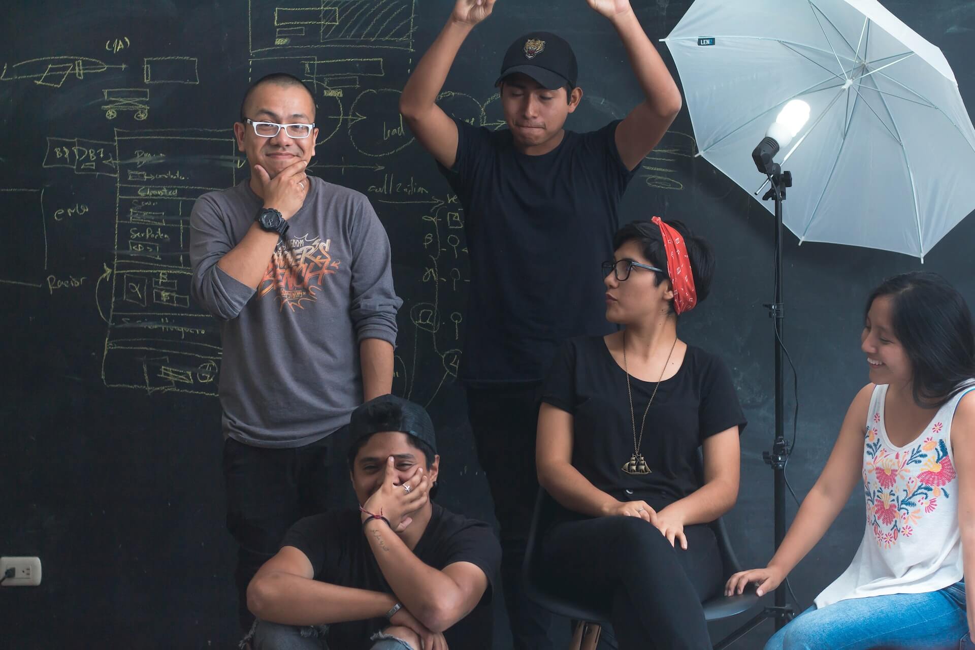 A team in a studio. They're in front of a blackboard, doing funny faces
