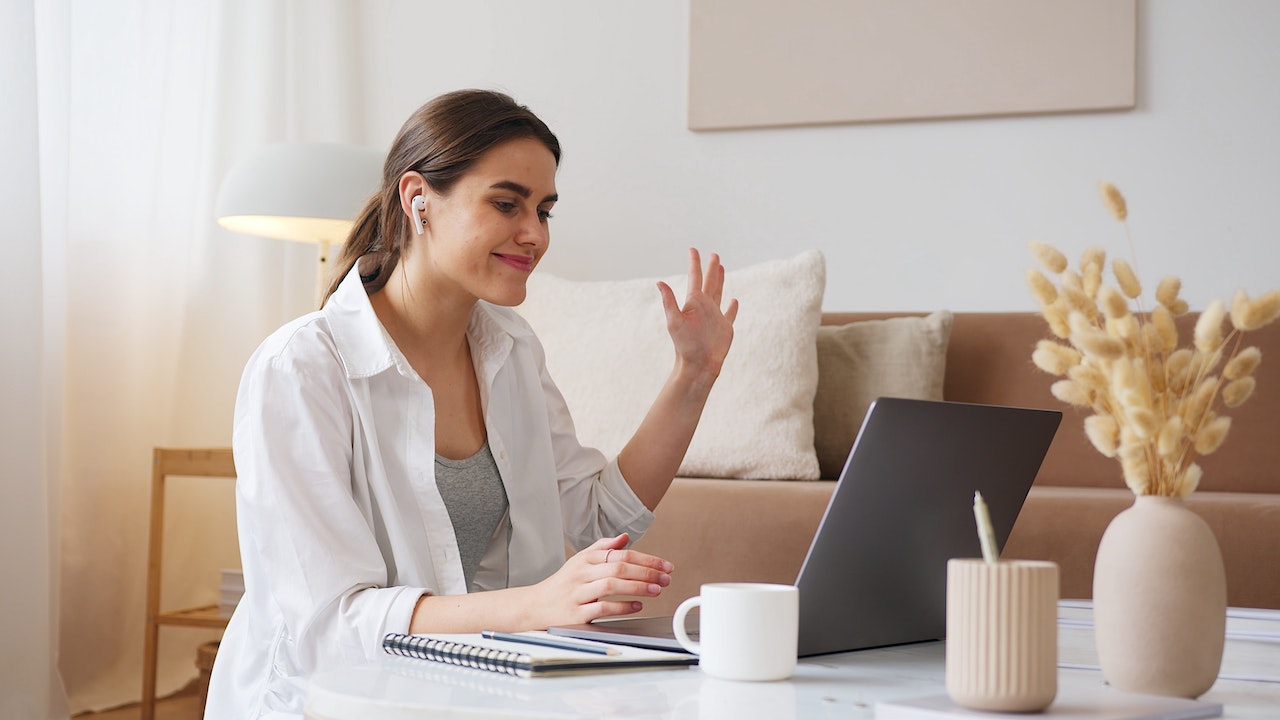 A woman smiling and waving at someone during a videocall
