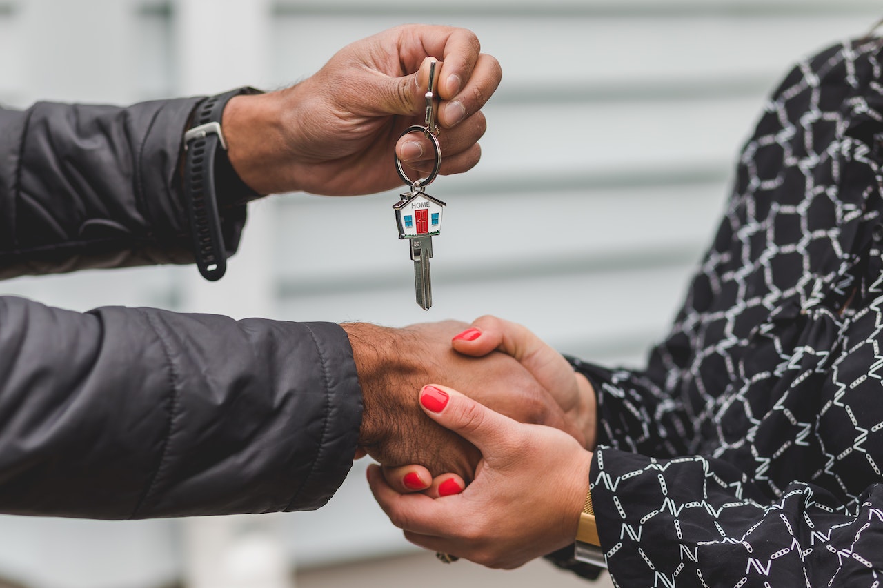 A realtor handing over the keys to homeowners on a keychain shaped like a house