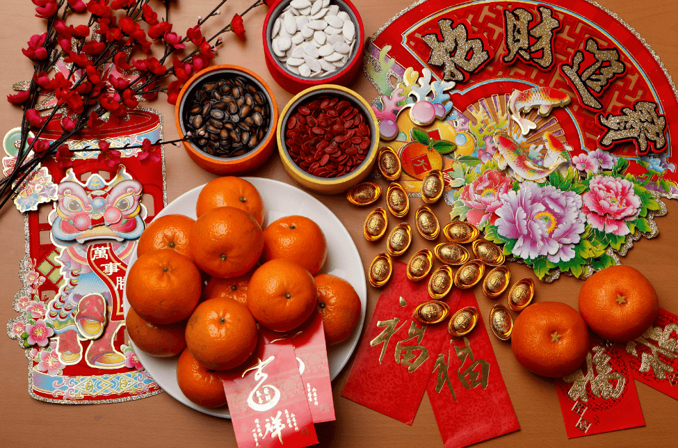 A spread of food, gifts, and items commonly seen in Chinese New Year, from envelopes to oranges.