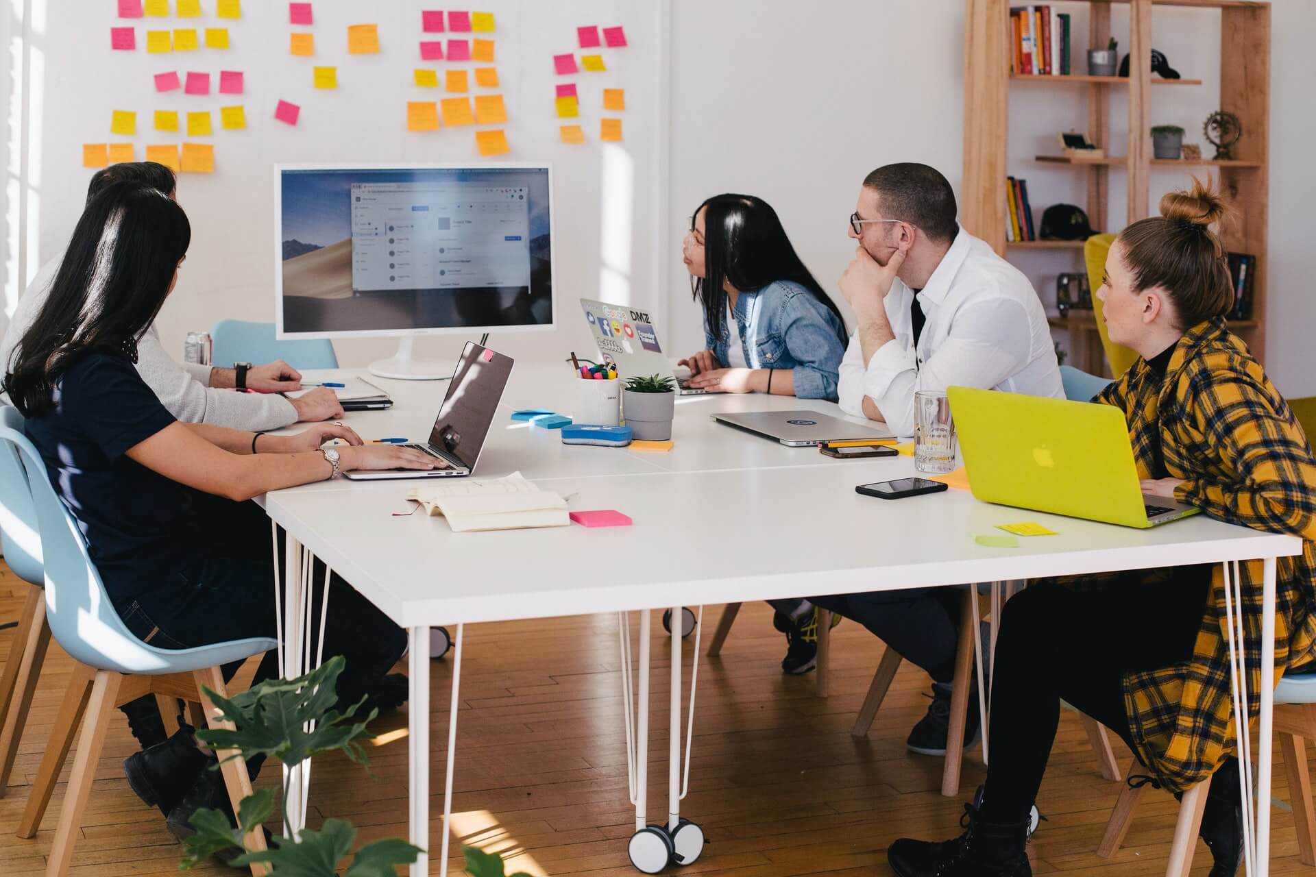 A marketing team, viewing a presentation on a screen. In front of them is a whiteoard full of pink, orange, and yellow sticky notes