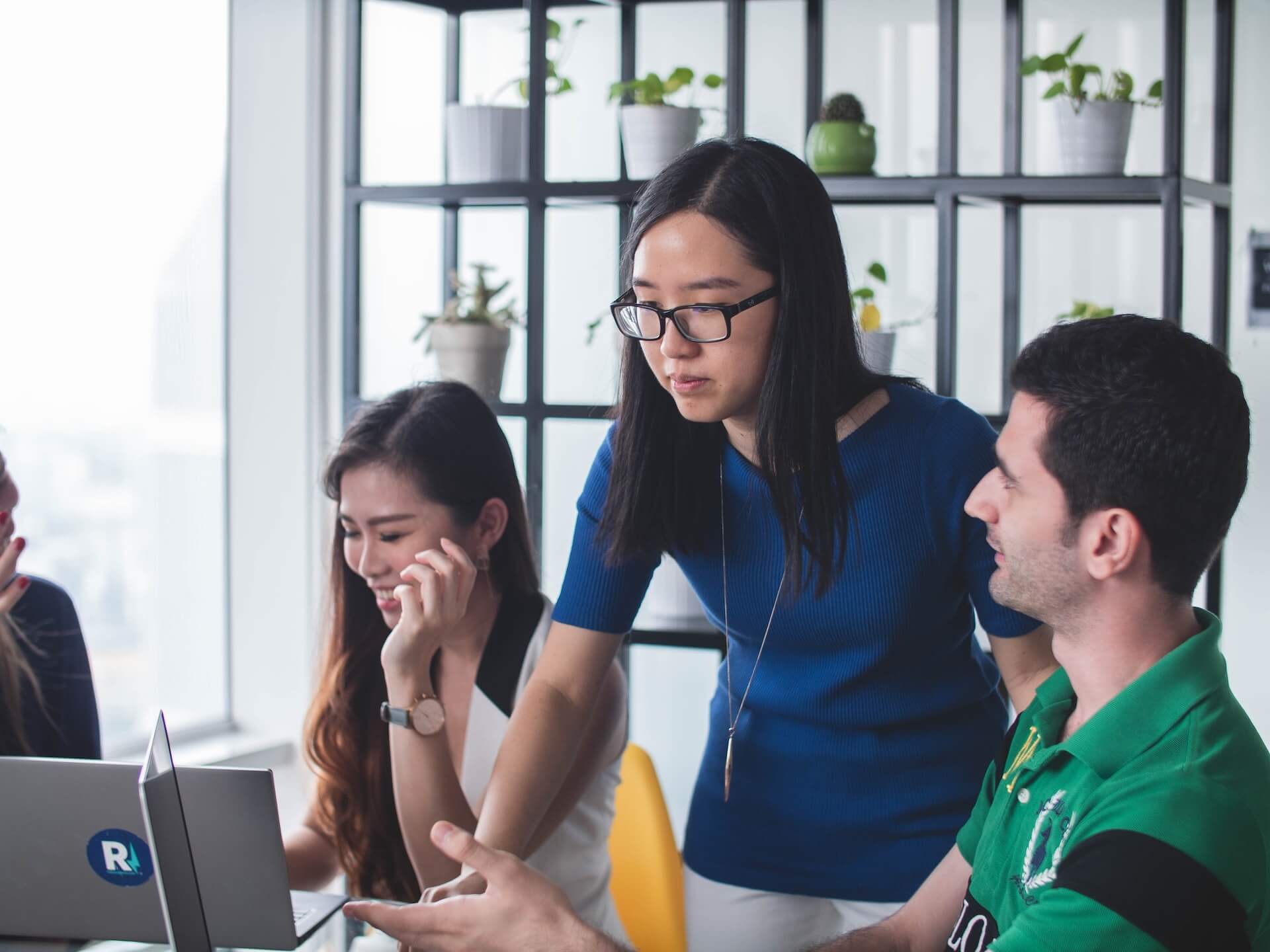 An Asian woman in glasses and a blue shirt showing her colleagues something on the computer